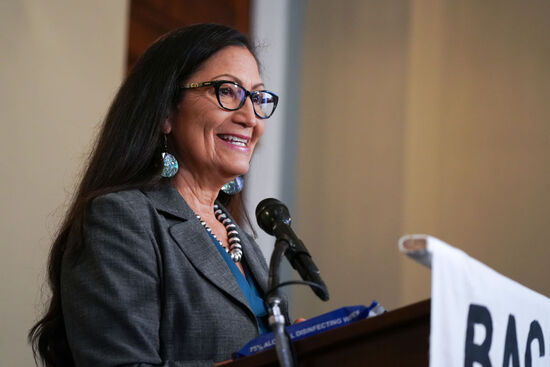 Deb Haaland. Secretary of the Interior. Standing, smiling from behind microphone/podium.
