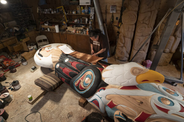 A man carving a special horizontal totem pole.