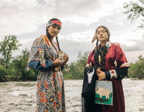 Indigenous youth in traditional dress standing in front of a river.